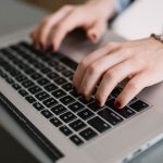 person using a laptop with writing tools, creative workspace